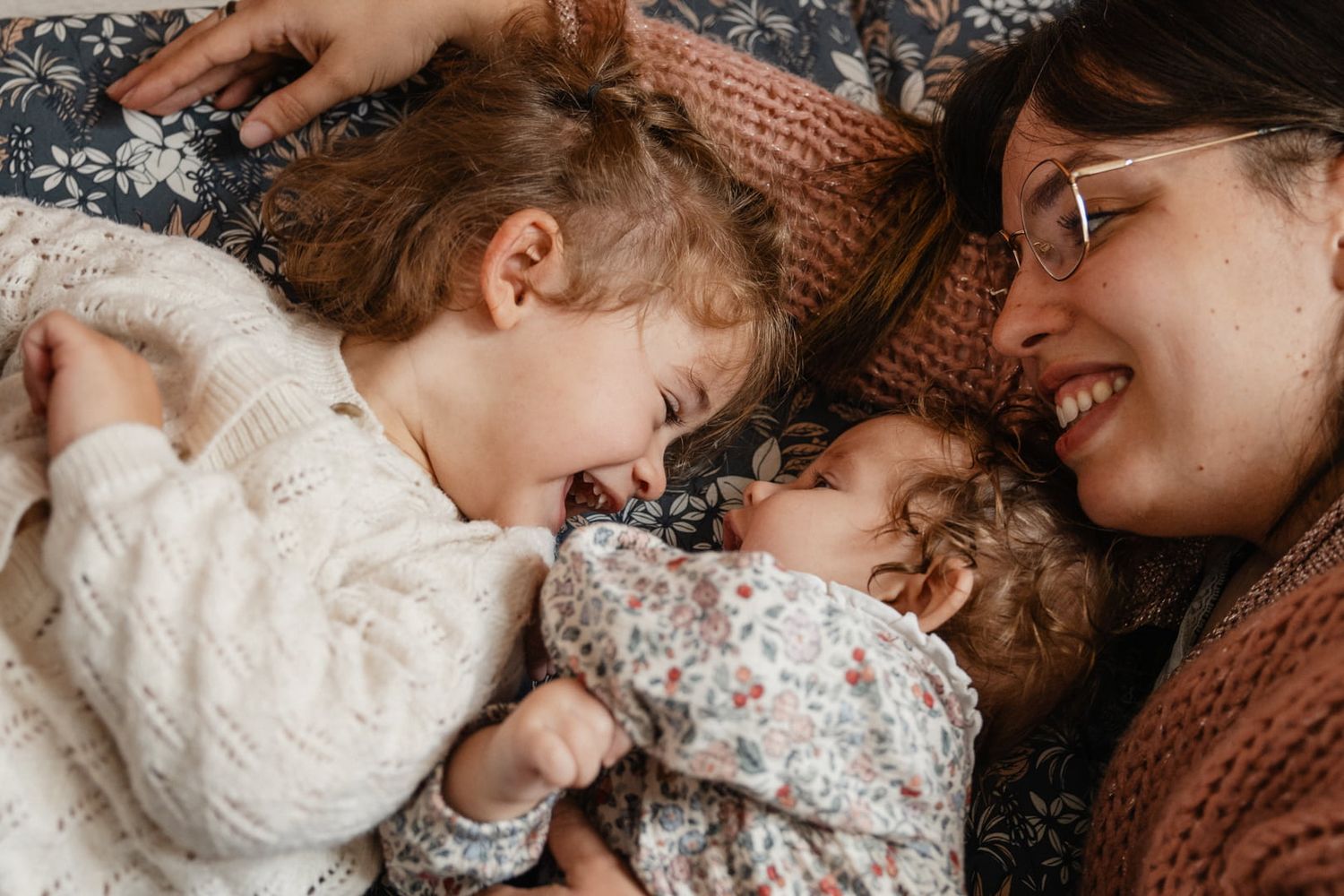 maman regarde la complicite entre ses filles echange de regard entre bebe et grande soeur en seance photo lifestyle à Lille