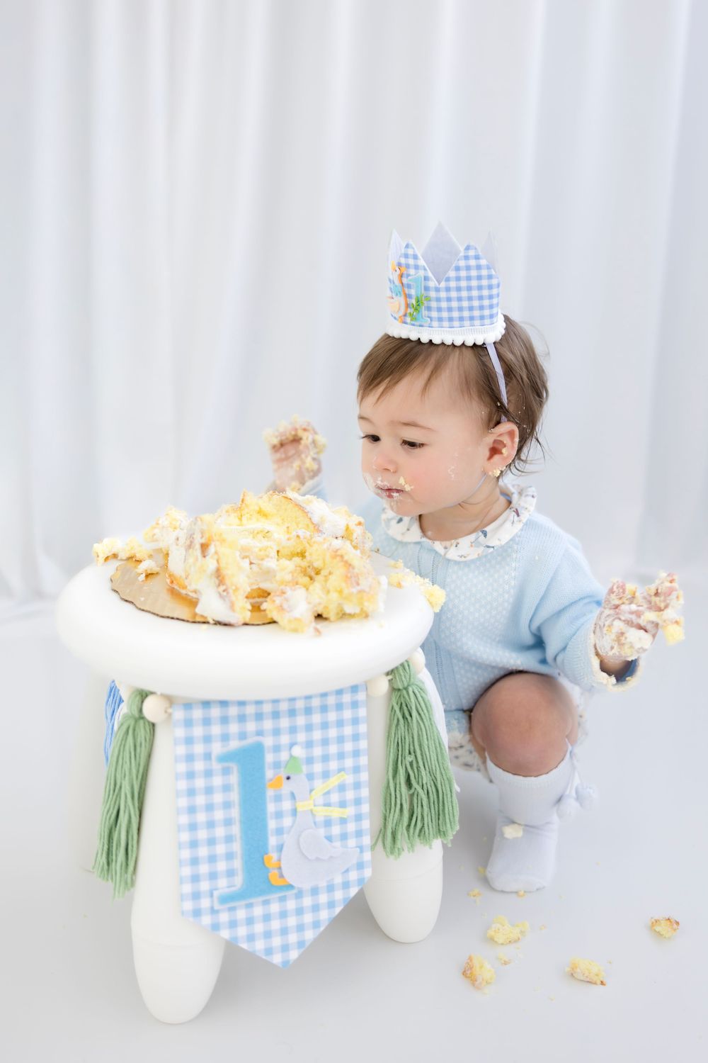 A baby boy in a blue crown celebrates his first birthday smashing a cake decorated with a duck theme.