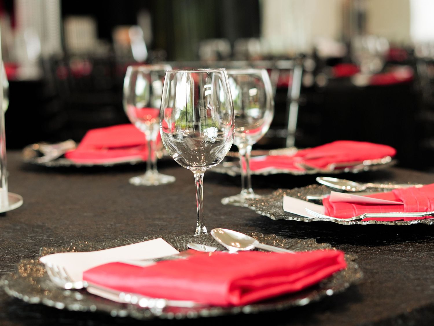 Elegant table setting with red napkins and wine glasses on black charger plates.