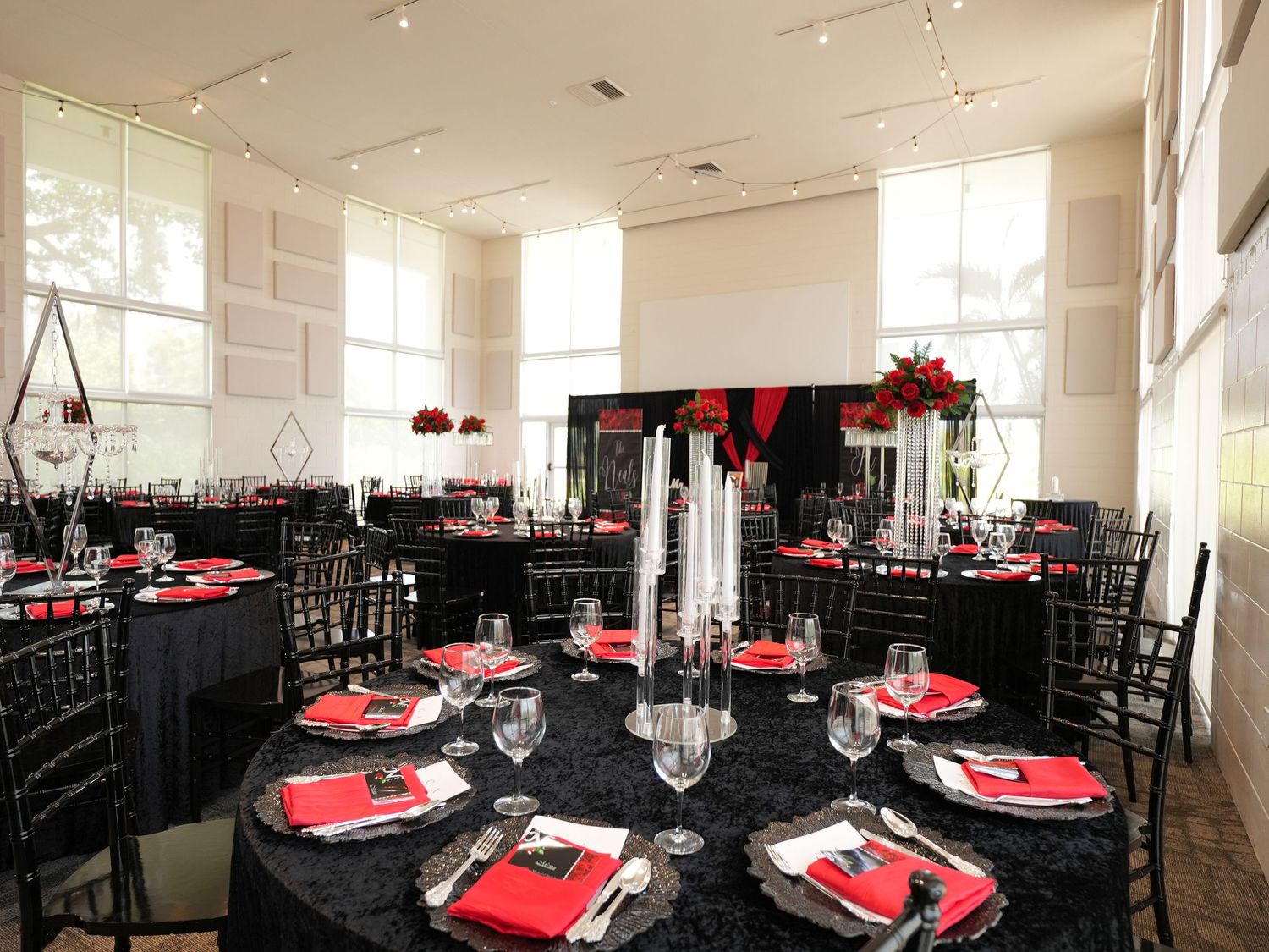 Modern event space with black and red table settings and tall floral centerpieces.