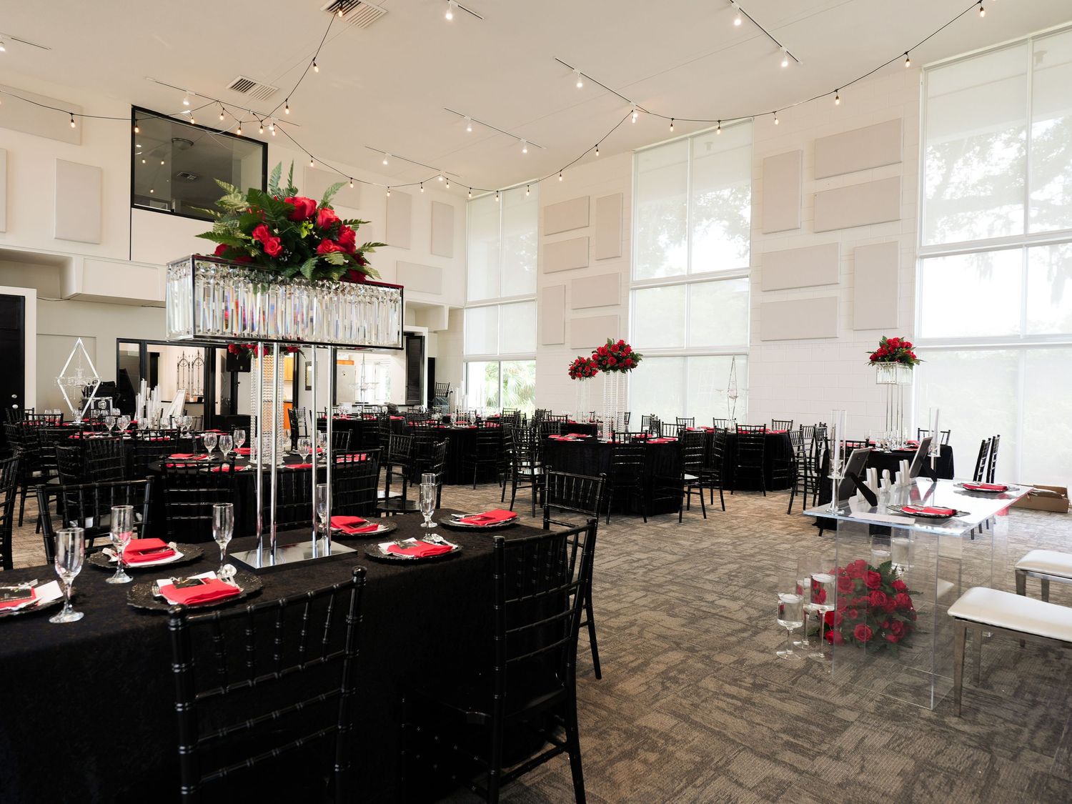 Spacious banquet hall decorated with black chairs and red accents for an elegant occasion.
