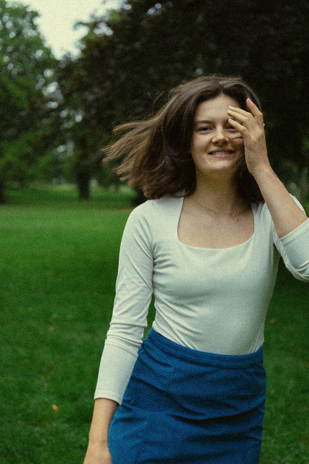 Portrait einer lächelnden Frau, die sich im Park auf grüner Wiese dreht im Blüherpark Dresden - Fotoshooting im Grünen