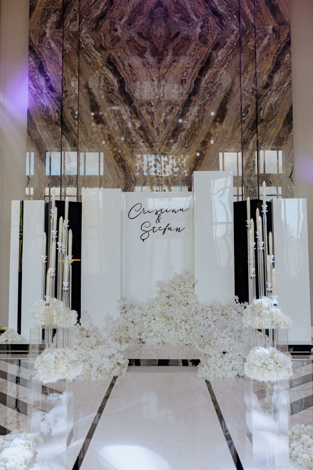 Elegant wedding ceremony setup with white aisle runner, floral arrangements and mirrored ceiling decor in modern venue.