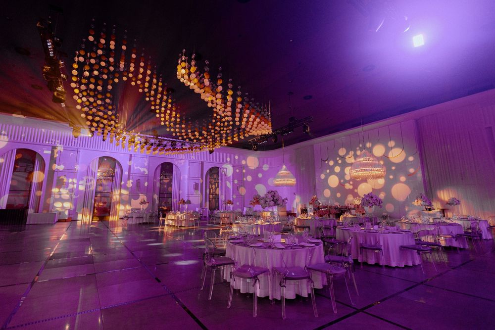 Wedding reception venue decorated with purple lighting and string lights creating a romantic ambiance in an elegant ballroom.