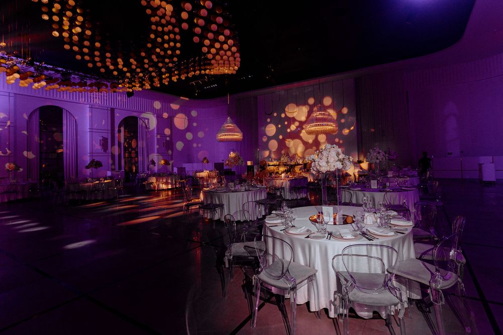 A luxurious wedding reception venue with purple uplighting, elegant table settings, and hanging string lights creates a romantic ambiance.