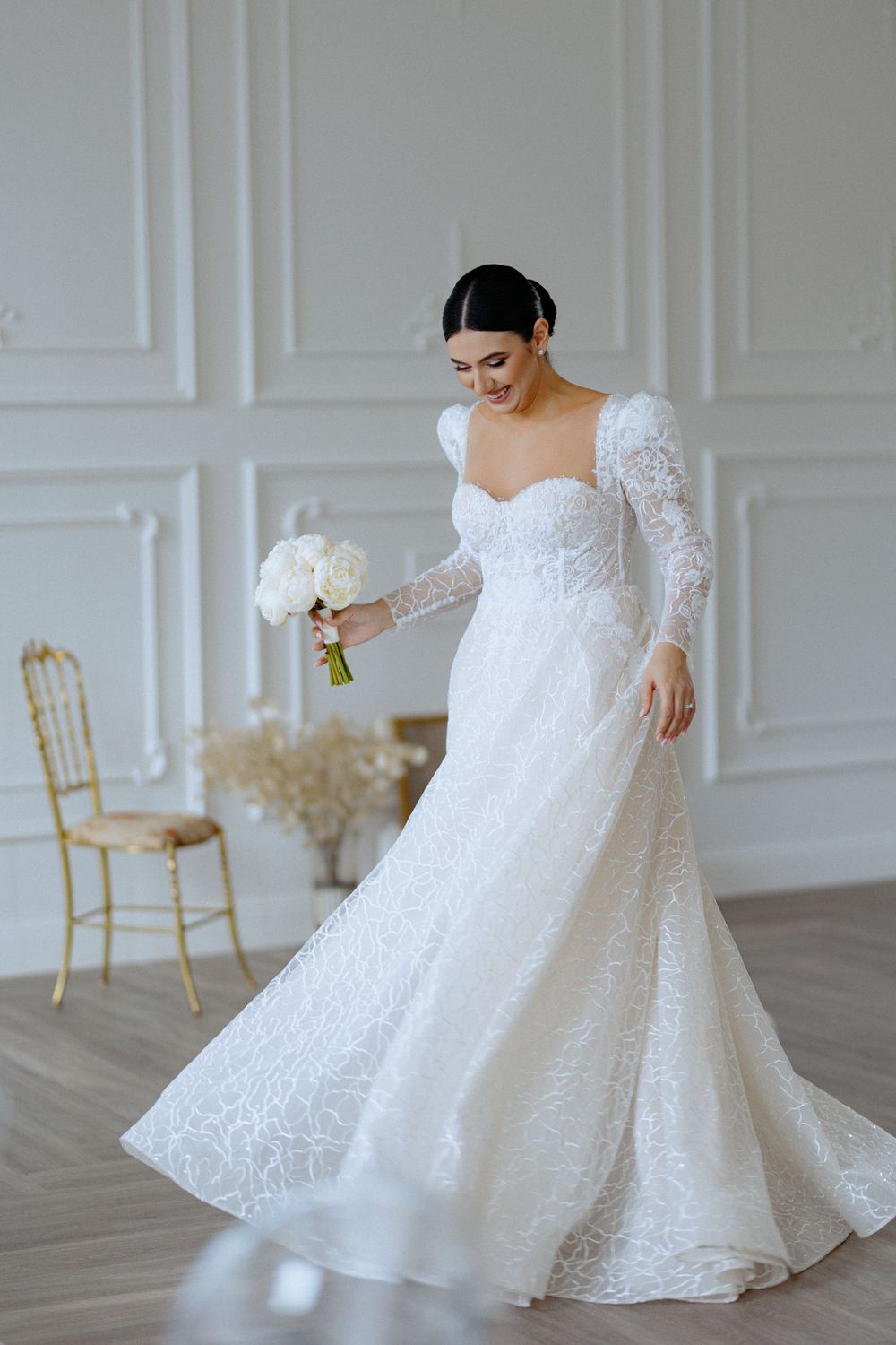 A stunning white lace wedding gown with long sleeves and sweetheart neckline shown in an elegant white room.