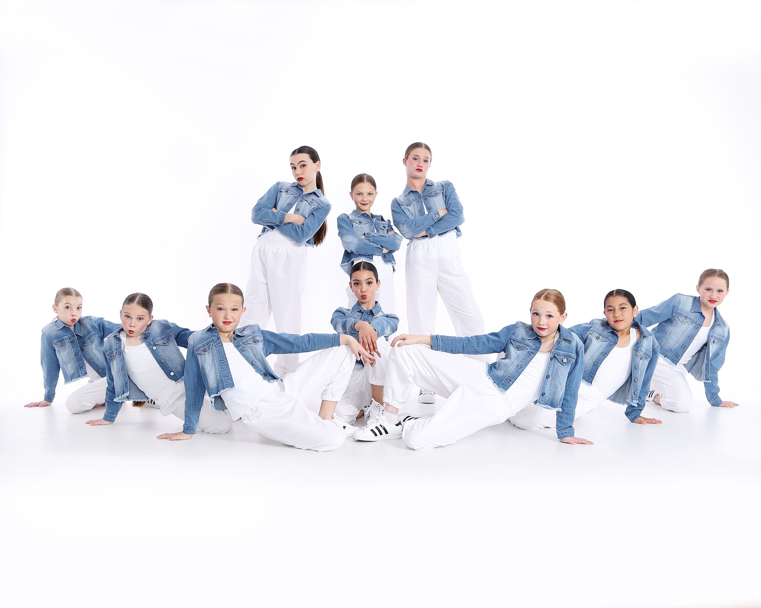 Dance group wearing matching denim outfits poses together in creative formation against white background for studio photo.
