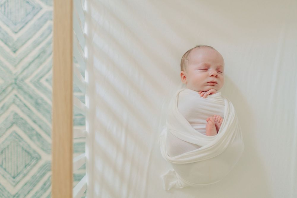 A newborn baby swaddled in white fabric lies serenely against a neutral background in a minimalist setting.