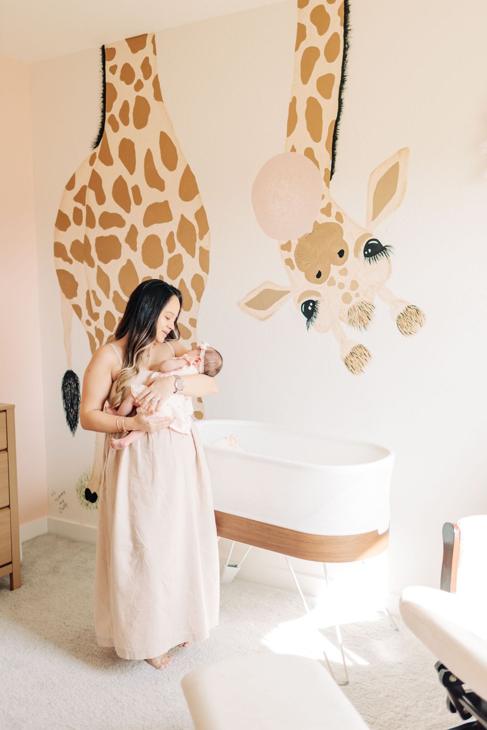 Intimate moment of mom holding her baby in the nursery with soft pastel colors and giraffe wallpaper behind.
