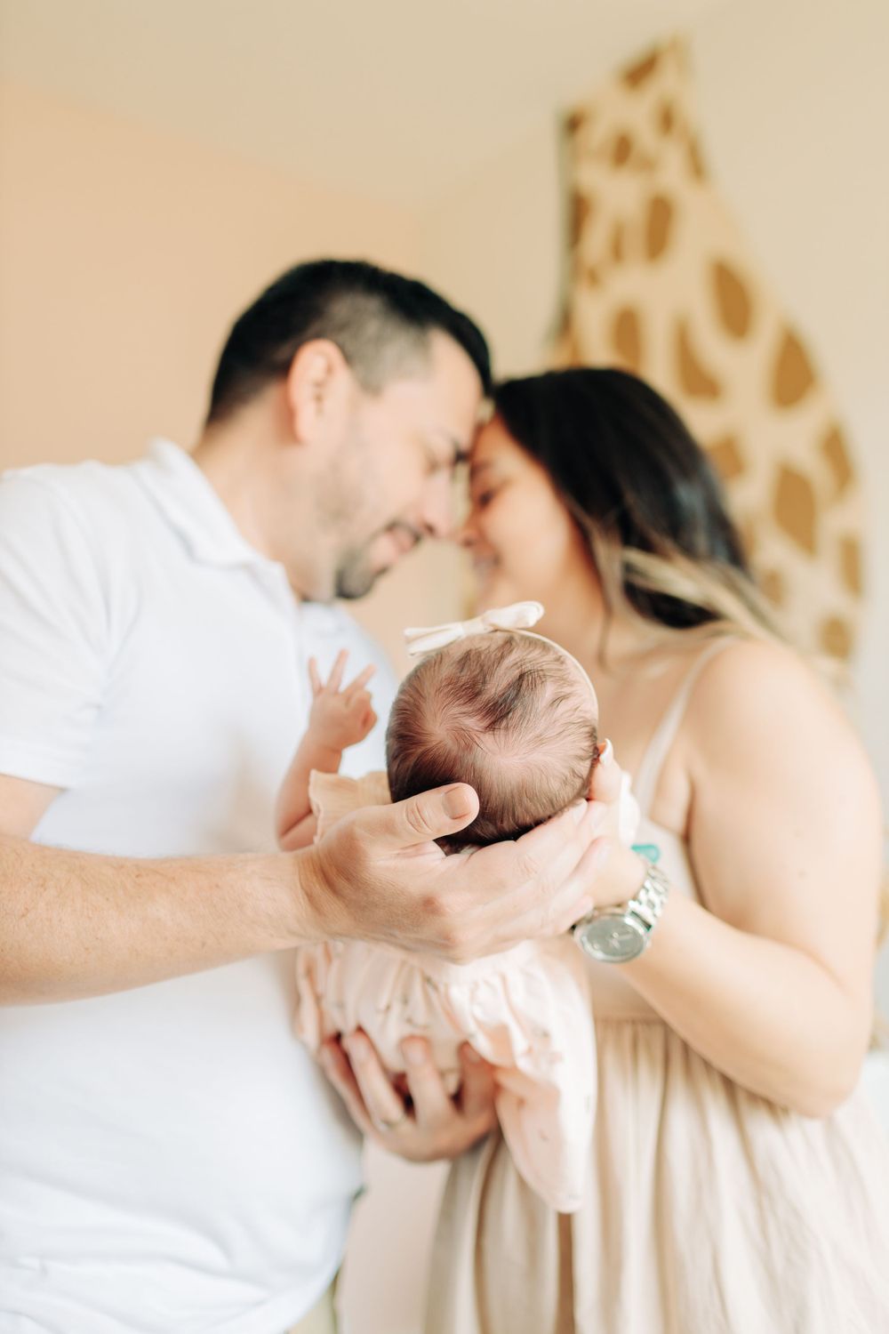 Mom and dad touching foreheads while holding their baby girl during a newborn session.