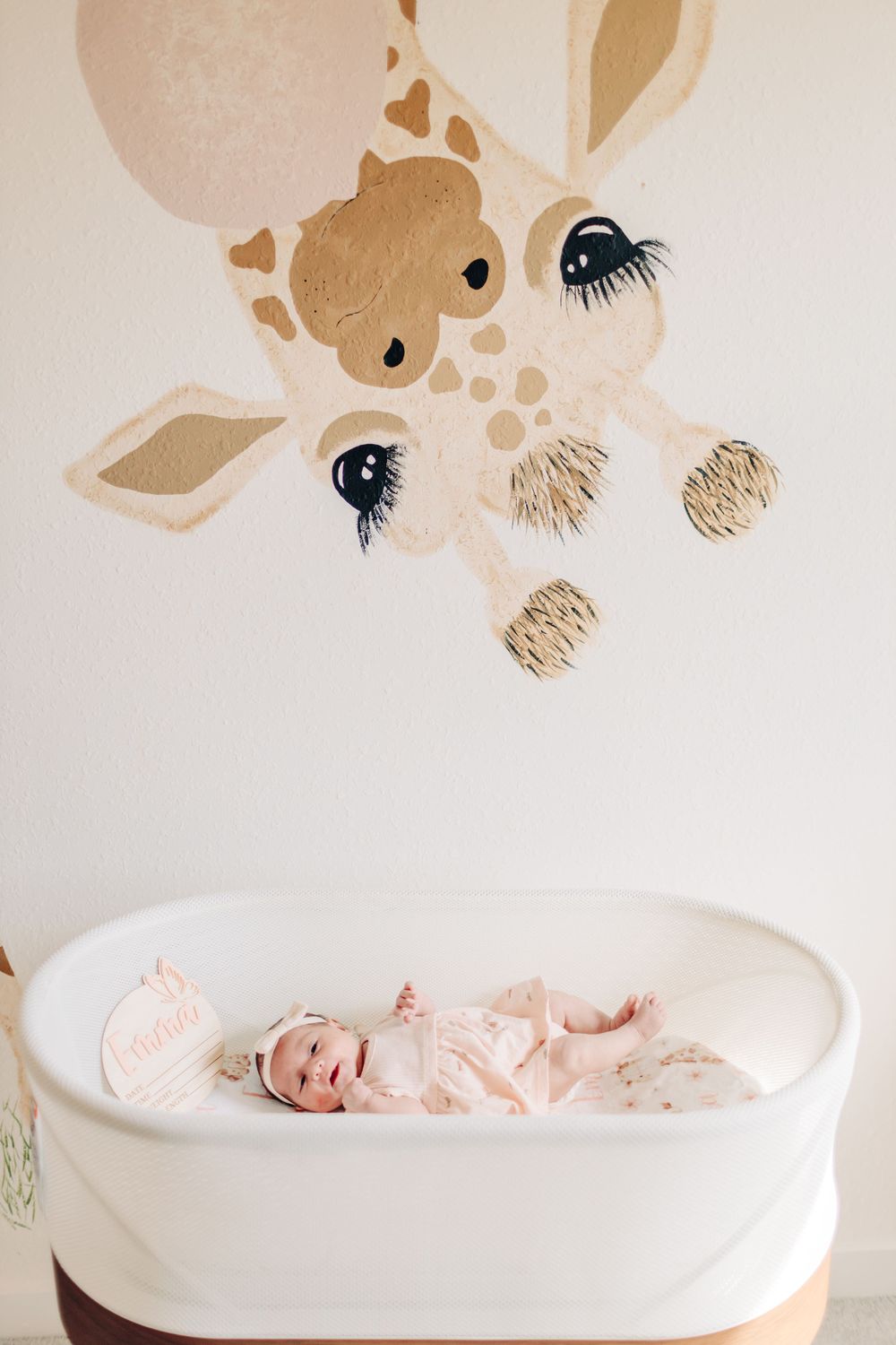 Baby laying in a white crib with a giraffe wallpaper above