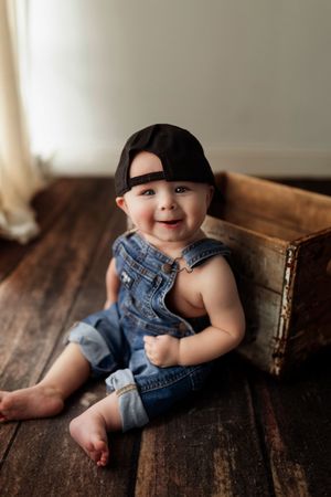A baby wearing denim overalls lies on a rustic wooden floor in a series of playful poses.
