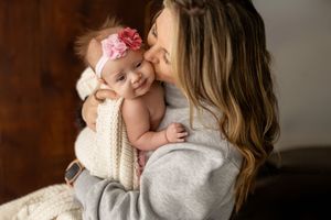 A tender moment between parent and newborn baby in a dimly lit room with soft natural light.