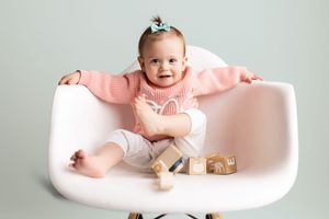A baby rests in a pink infant bath lounger with wooden toys nearby.