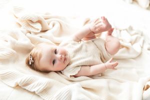 Newborn baby wearing cream colored knit clothing lies on soft white textured blanket during professional photo session.