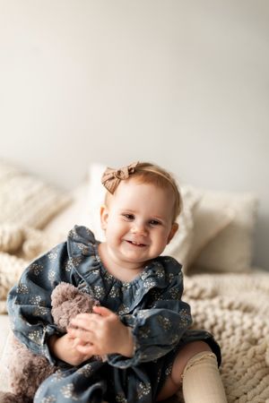 Baby wearing navy floral dress lies on cream textured blanket while smiling and playing.