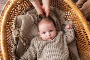 Baby in knit sweater lying in woven basket with hand reaching in frame.