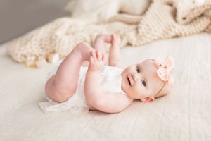 Baby wearing peach bow lying on white blanket.