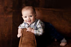 Cheerful infant peeking over brown leather furniture against dark background.