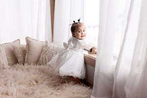 Small child in white outfit sitting on curved white rocker against light background.