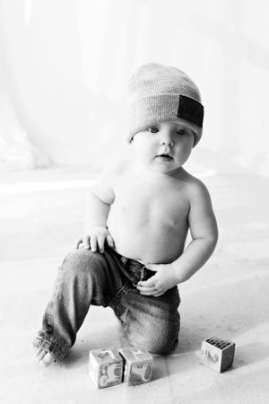 Baby wearing gray beanie and shorts sitting on white background.
