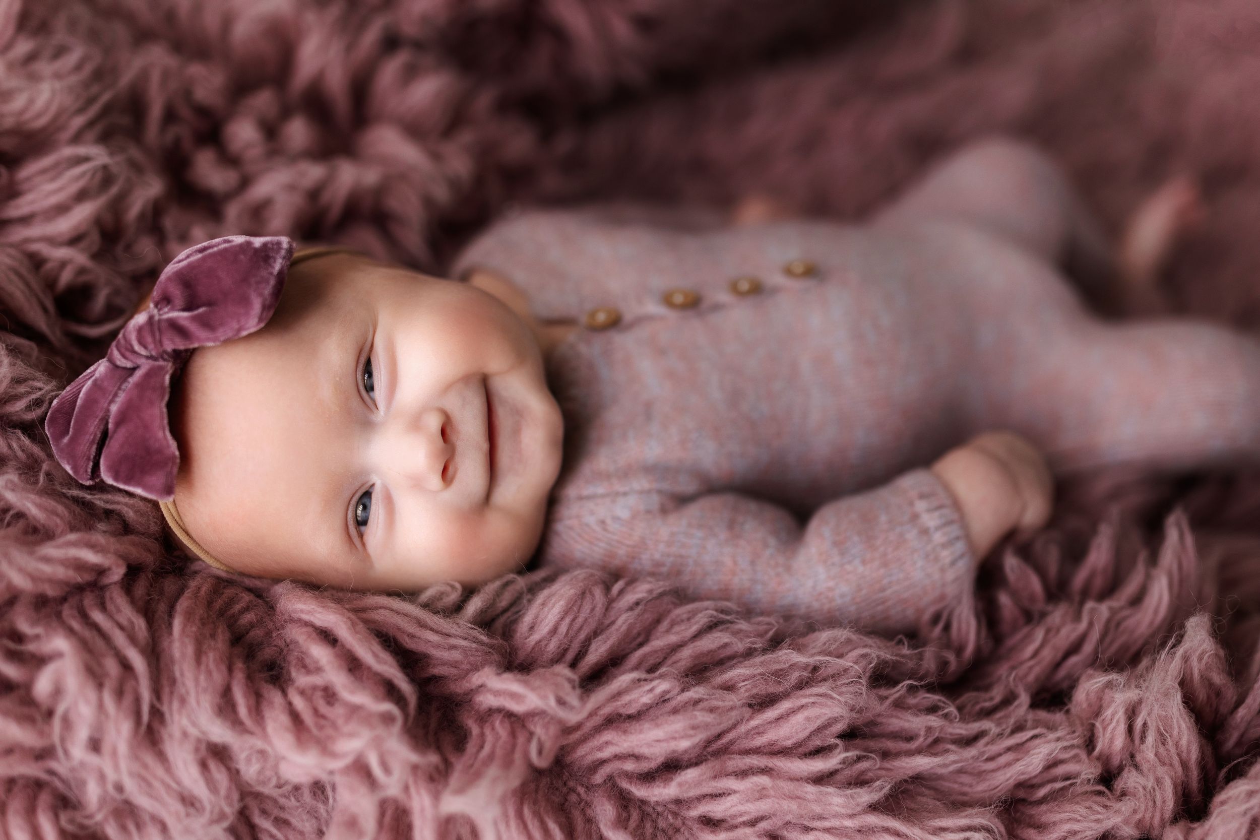 Artistic newborn photography on mauve fabric with gentle studio lighting.