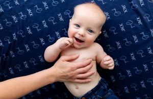 A happy baby lying on a navy patterned blanket smiles while hands support them.