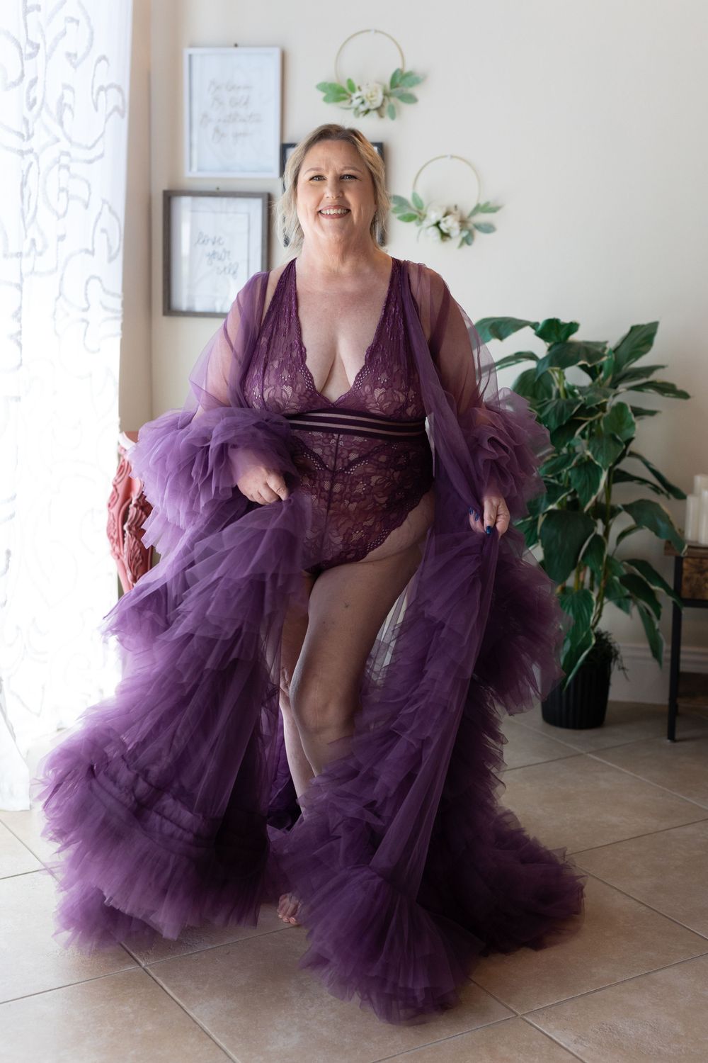 Person wearing flowing purple tulle robe and lingerie in front of decorative wall art.