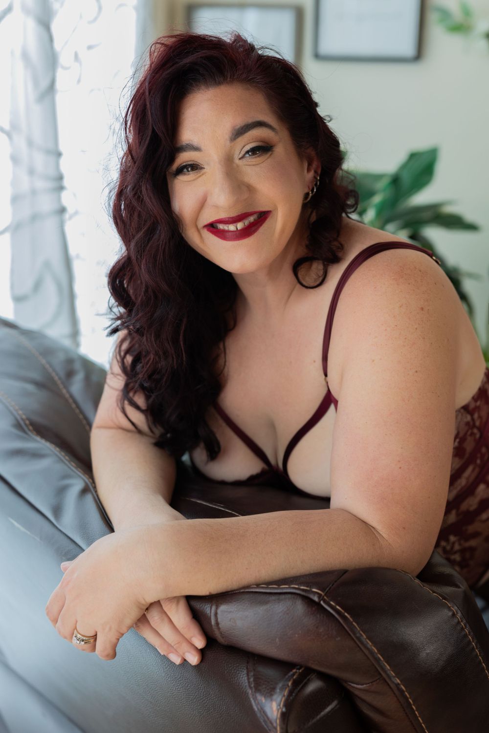 Portrait of a person in burgundy lingerie lounging on a leather sofa.