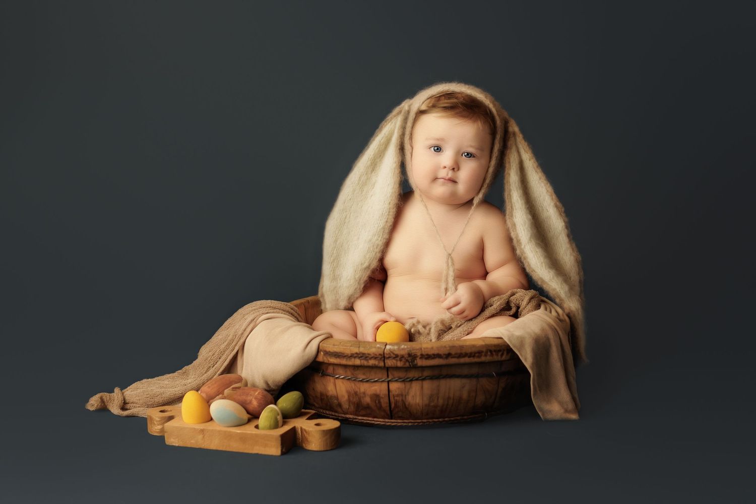 Artistic studio portrait showing a baby seated in rustic brown and beige tones with natural props and dark backdrop.