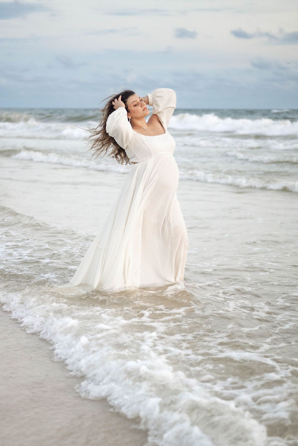 Wind-swept white dress contrasts against stormy beach backdrop during coastal photoshoot.