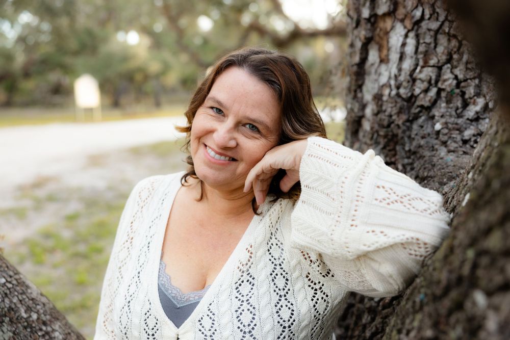 Casual outdoor portrait of someone in white sweater leaning against tree.