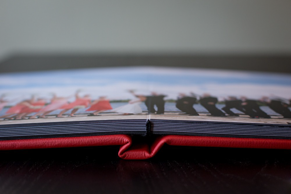Close-up of open wedding photo album with red leather cover on dark wooden surface.