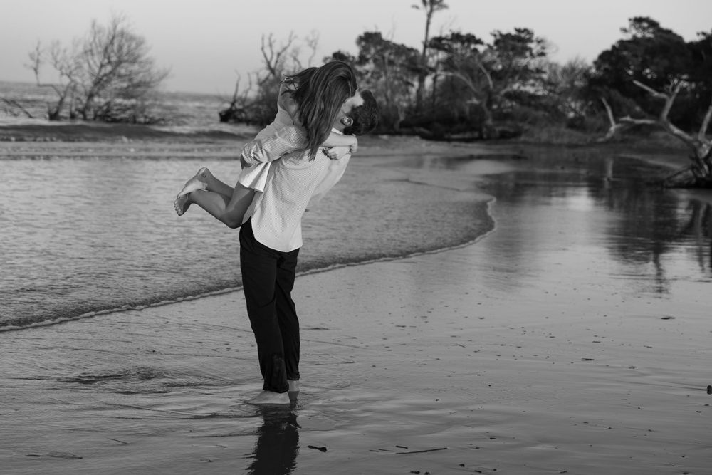 A joyful black and white photo of a couple playing in shallow water captured by Charleston photographer.