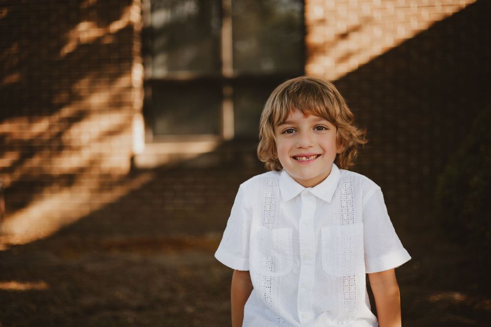 Young student in white collared shirt smiling brightly in sunlit outdoor setting captured by Charleston photographer.