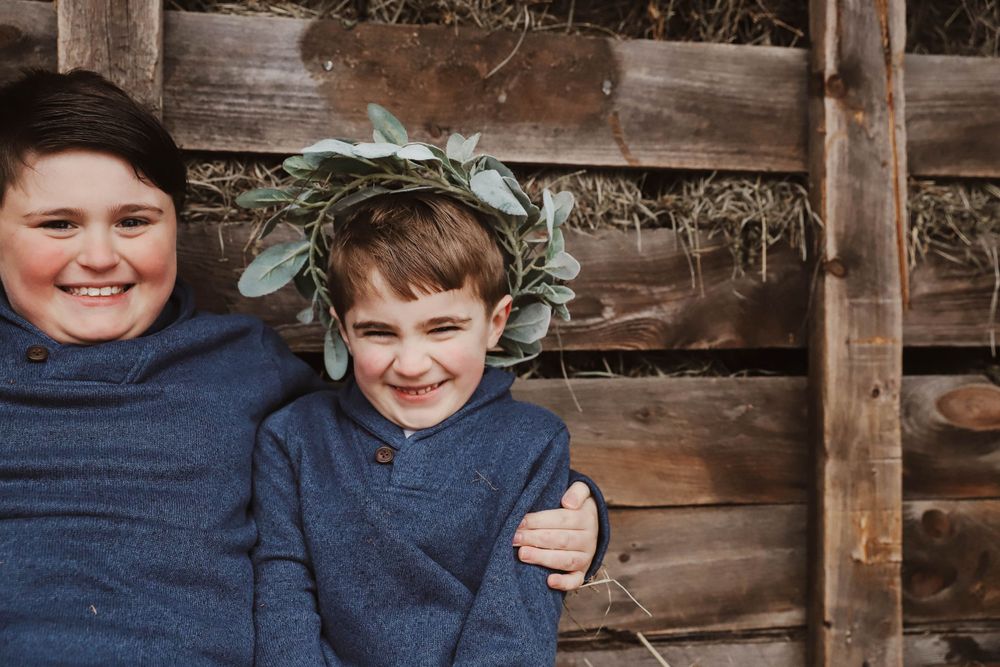 Two children sitting together against rustic wooden wall, one wearing a leafy crown captured by Charleston photographer.