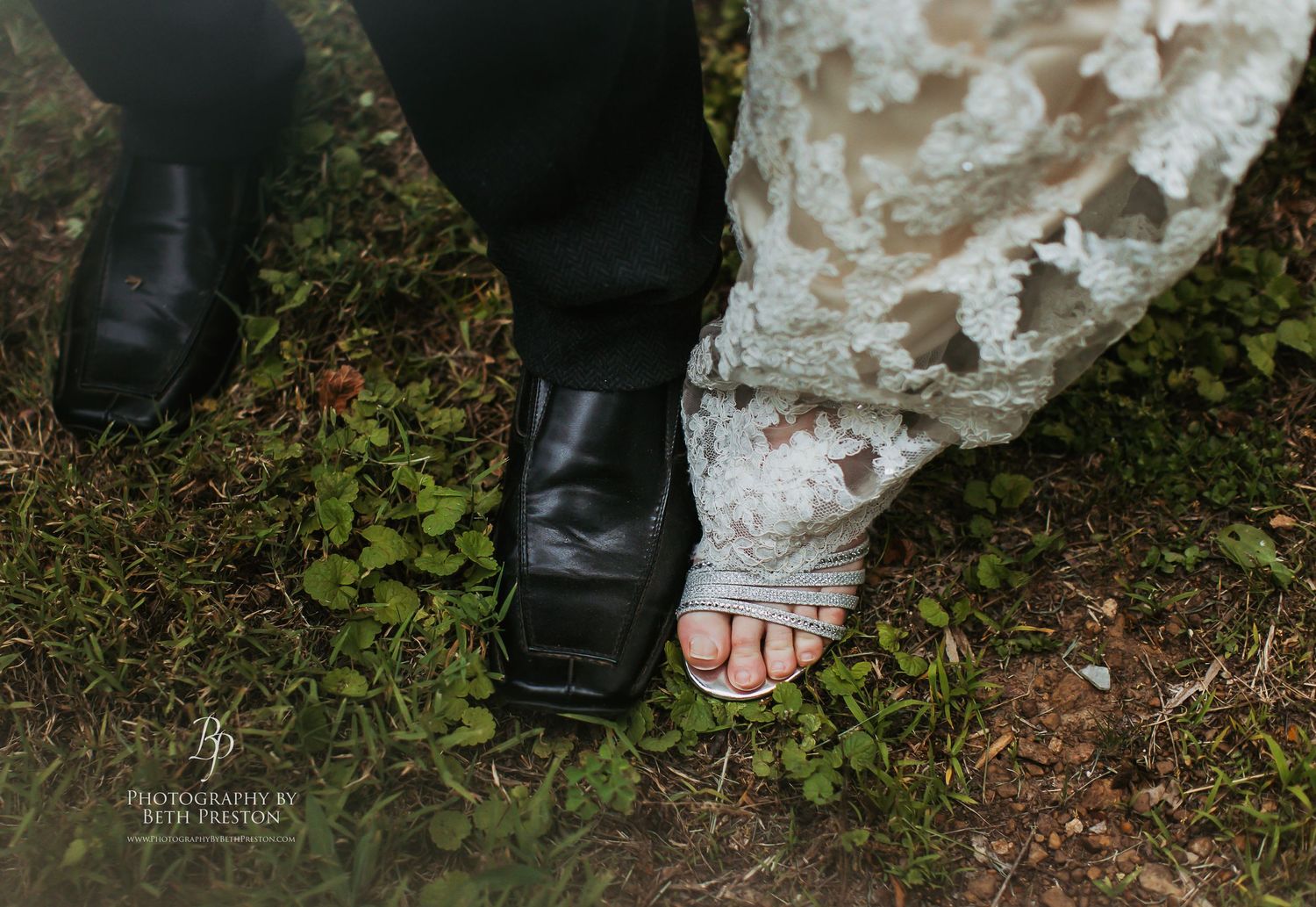 Wedding detail shot showing dress lace and formal shoes on mossy ground.