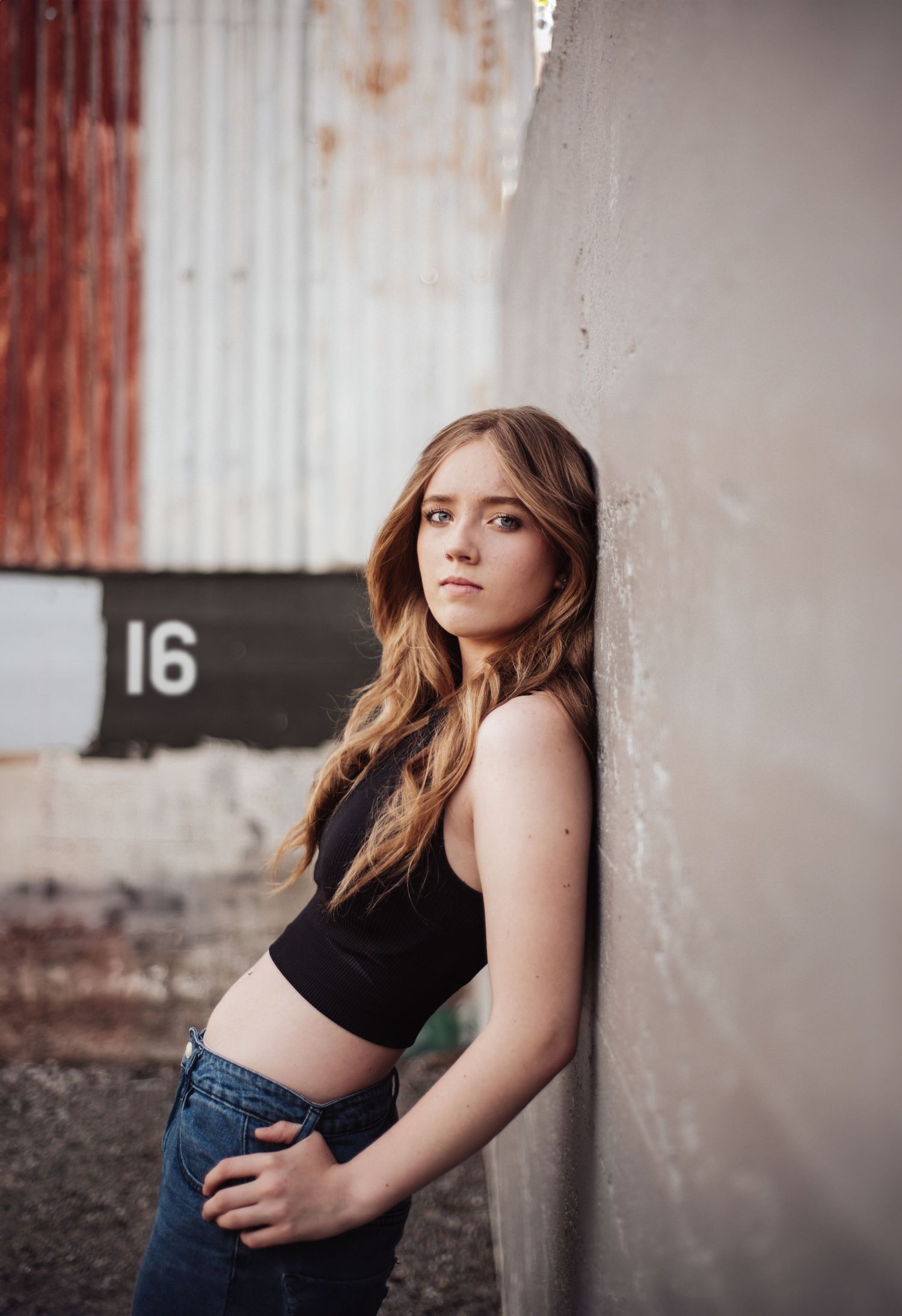 Urban portrait against industrial wall with number 16 visible.