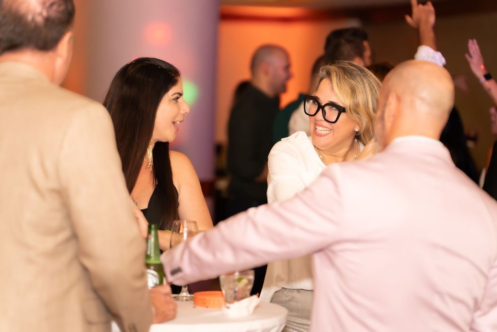 People gathering at an indoor social event with warm lighting and drinks, having animated conversations at a table.
