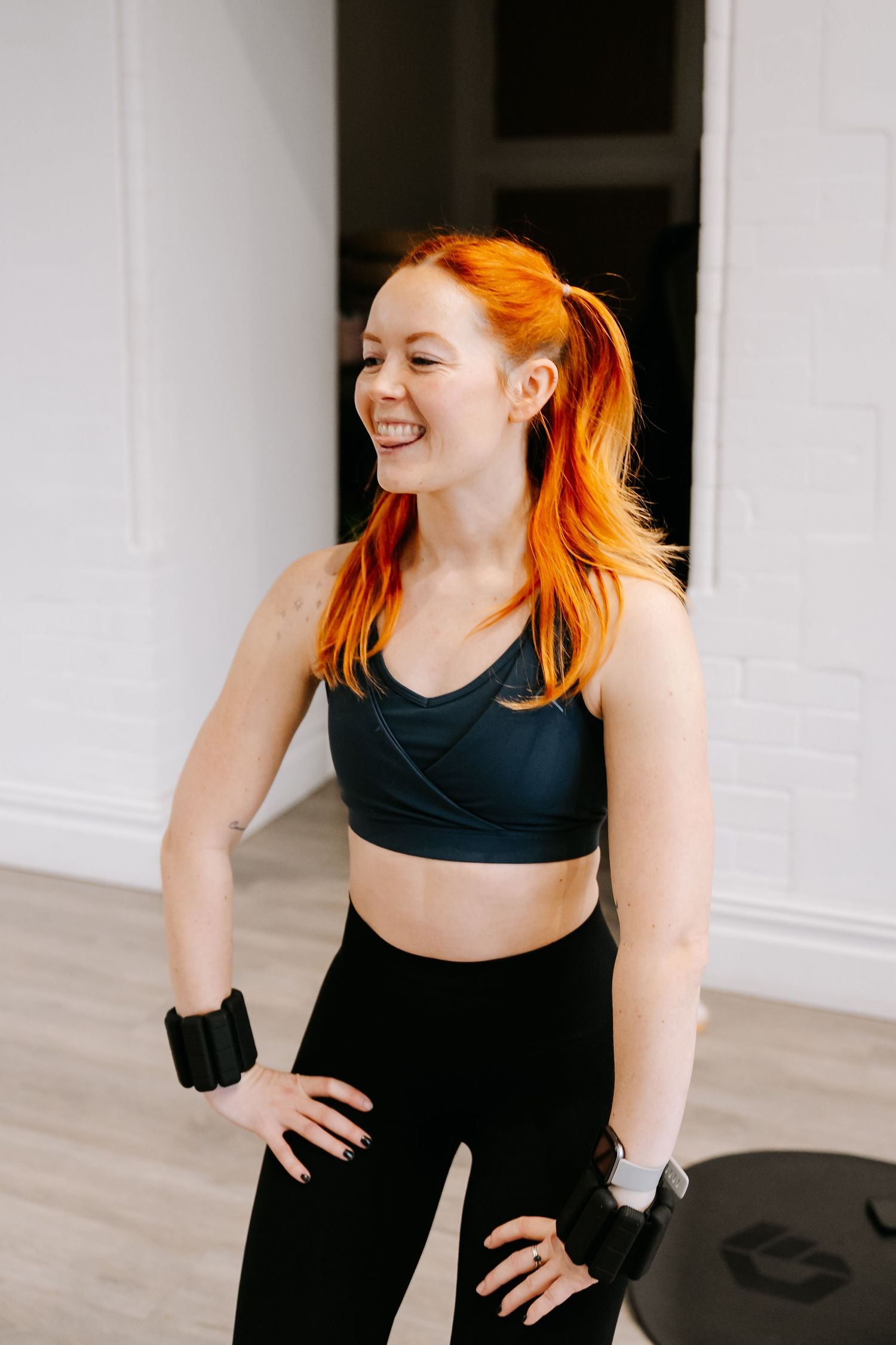 A person in black workout attire smiles and dances during an energetic fitness session in a bright studio space.