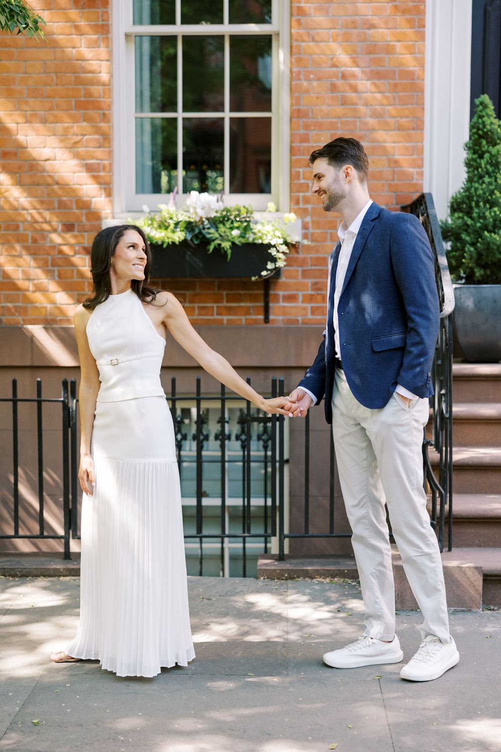 Couple in coordinated white and navy outfits pose in front of historic brownstone with window planters in New York City.