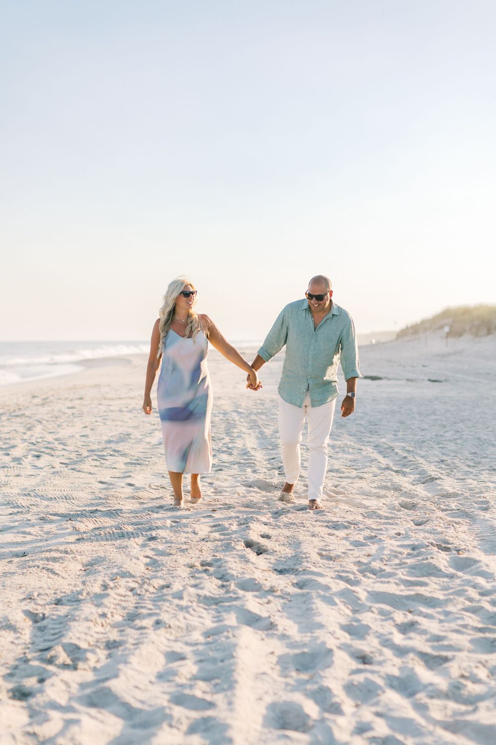 A couple walking hand in hand on a white sandy beach at sunset.