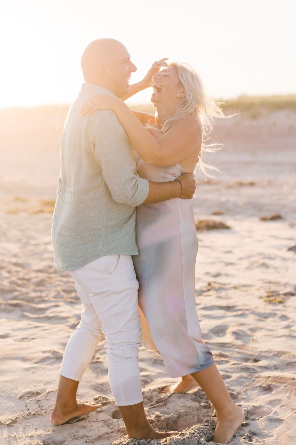 A couple dancing together barefoot on a sandy beach during golden hour.