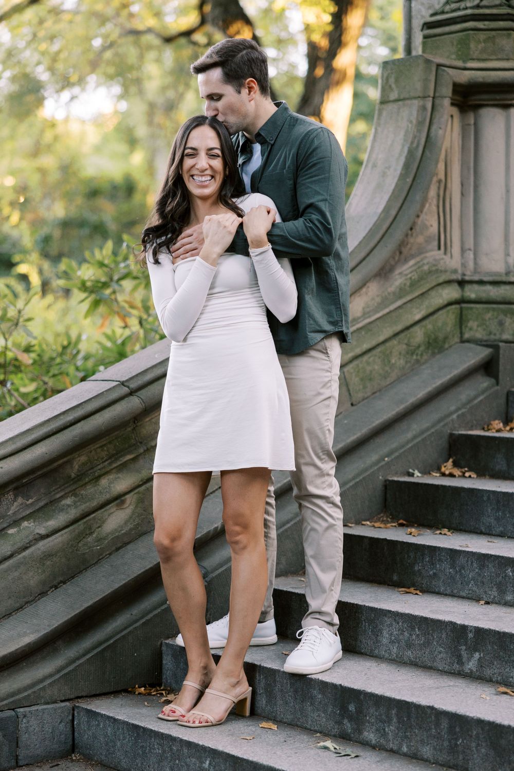 A couple poses intimately on stone steps during an outdoor engagement photoshoot.