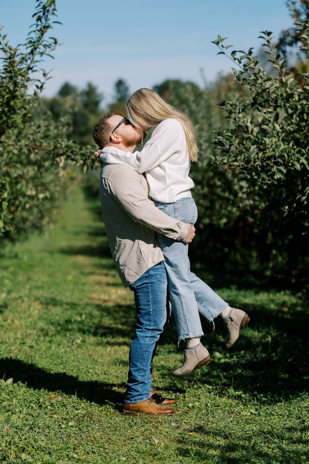 A romantic couple embraces in an apple orchard on a sunny autumn day.