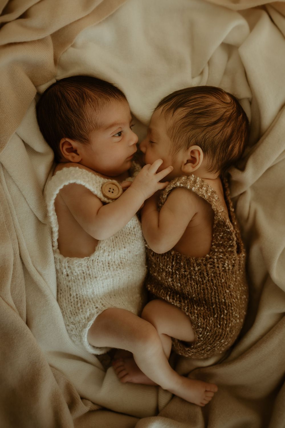 A peaceful sleeping newborn wrapped in a soft knit blanket grasps a gentle hand.