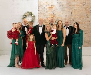 Holiday family photo with people wearing emerald green dresses and formal black tuxedos.
