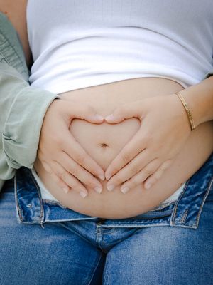 A series of photos showing the progression of a pregnant belly growing larger over time, wearing jeans and a white top.