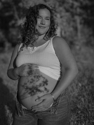Black and white maternity photo series showing a pregnant woman in a white tank top and jeans against a natural background.