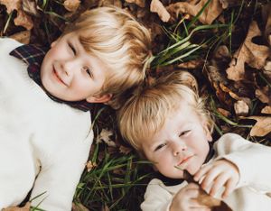 A figure lying in autumn leaves wearing a white sweater during a fall photoshoot.